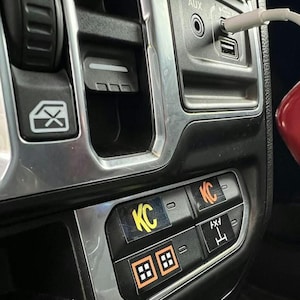 May include: Close-up of a car's interior with a silver trim and black dashboard. There are several buttons, including two labeled "KC" and one labeled "4x4".
