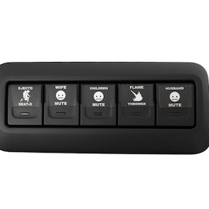 May include: Black control panel with five buttons. Buttons are labeled "EJECTO SEAT-O", "WIFE MUTE", "CHILDREN MUTE", "FLAME THROWER", and "HUSBAND MUTE". Each button has a corresponding graphic.