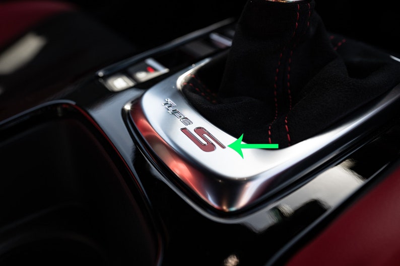 May include: Close-up of a black leather car gear shifter with red stitching. The gear shifter has a silver trim with the word "Sport" and the letter "S" in red.