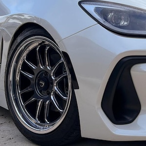 May include: A white Subaru WRX with black fender flares and aftermarket wheels. The wheels are silver with black accents and the text "Rays Racing" is visible on the wheel.