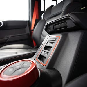 以下が含まれることがあります： 赤いステッチが施された黒い革の車のインテリアのクローズアップ。センターコンソールには、赤と黒のコントロールノブと、複数のボタンがついたパネルがあります。