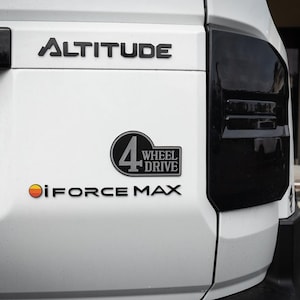Pode incluir: Veículo branco com um emblema preto "ALTITUDE", um emblema preto "4 WHEEL DRIVE" e um emblema preto "iFORCE MAX".
