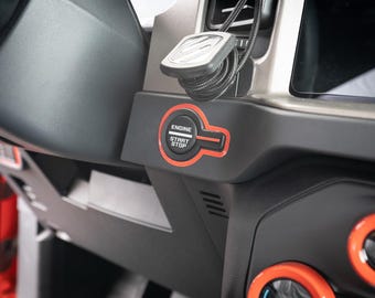 May include: Close-up of a black car interior with a red engine start/stop button. The button has the words "Engine Start Stop" printed on it.