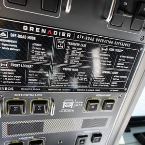 May include: An overhead vehicle control panel for the Grenadier featuring a carbon fiber patterned instruction placard for off-road operation. The panel includes black toggle switches for differential locks and off-road modes with white text labels.