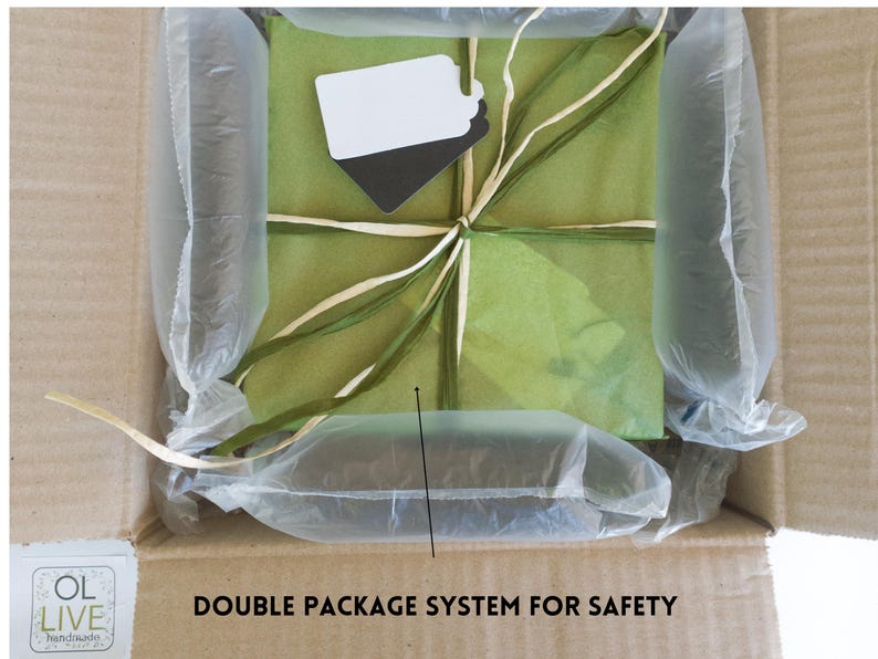 May include: A brown cardboard box with a green and white gift wrapped inside. The gift is wrapped in tissue paper and tied with a ribbon. The box is filled with air-filled packaging to protect the gift during shipping. The text "DOUBLE PACKAGE SYSTEM FOR SAFETY" is printed on the box.