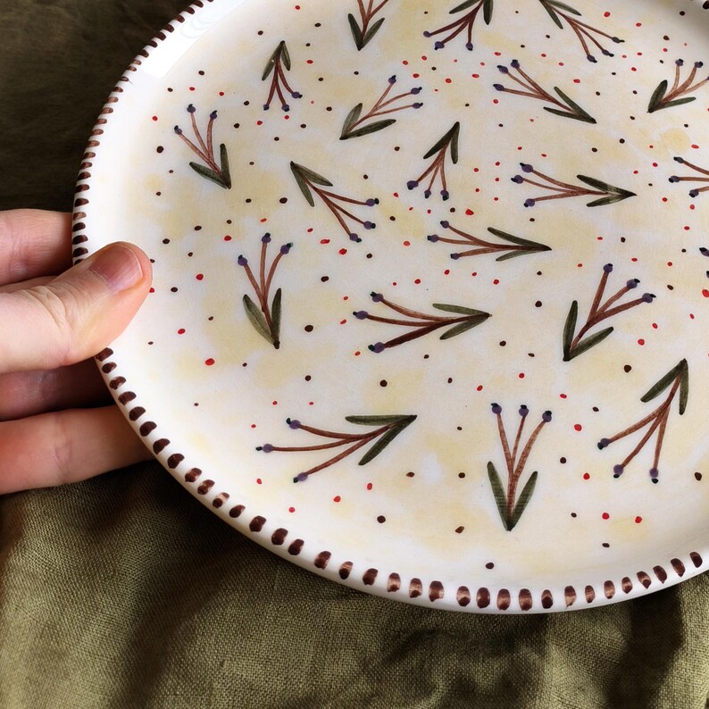May include: A white ceramic plate with a brown rim and a pattern of purple flowers and green leaves on a yellow background.