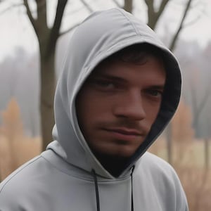 Puede incluir: Una sudadera con capucha de color gris claro que presenta un forro interior oscuro dentro de la capucha y dos cordones negros finos que cuelgan del cuello. La prenda está confeccionada con un tejido liso de color sólido y capucha estructurada.
