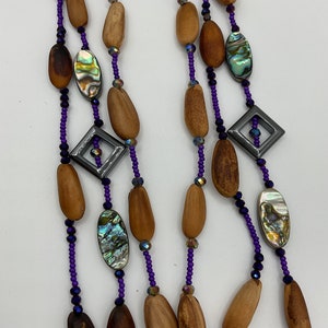Puede incluir: Un collar de múltiples hilos con cuentas de madera, detalles de concha de abulón iridiscente y cuentas de vidrio morado y negro.