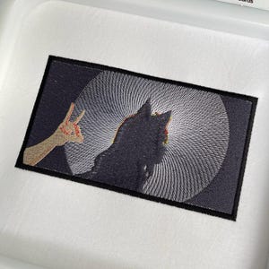 Op de afbeelding: Gestikt patch met een zwart-witte afbeelding van een persoon met een kroon op zijn hoofd. De persoon kijkt weg van de kijker en is omringd door een draaiende patroon. Het patch is omlijst met een zwarte rand.
