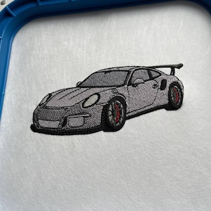 May include: Embroidered design of a gray Porsche 911 GT3 RS sports car with red brake calipers. The car is embroidered on a white fabric.