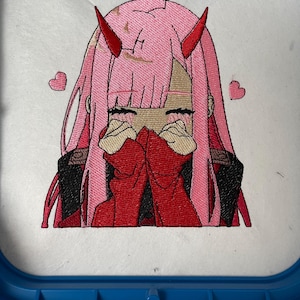 May include: Embroidered image of a pink-haired anime character with red horns and a red sweater, covering her face with her hands. Two pink hearts are on either side of the character.