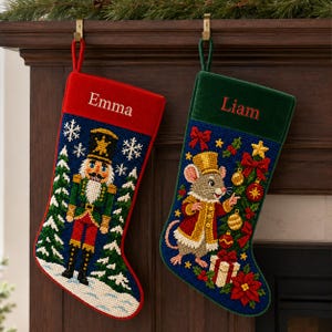 May include: Two personalized Christmas stockings with hanging loops. The left stocking is red with a nutcracker, snowflakes, and the name Emma. The right stocking is green with a mouse in a gold hat, ornaments, and the name Liam. Both feature needlepoint designs.