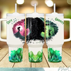 May include: Three white travel mugs with black handles and lids. Each mug features a different graphic design with a watercolor background. The first mug has a pink and green design with the text "DEFY". The second mug has a green and black design with the text "WH. I. I.". The third mug has a green and black design with the text "GRAVITY".