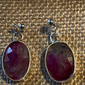 Może przedstawiać: Para srebrnych kolczyków z owalnymi, różowymi kamieniami. Kamienie są osadzone w srebrze i mają lekko fakturowaną powierzchnię.