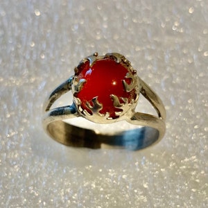 Può includere: Un anello d'argento con una pietra preziosa rossa incastonata in un design delicato e ornato.
