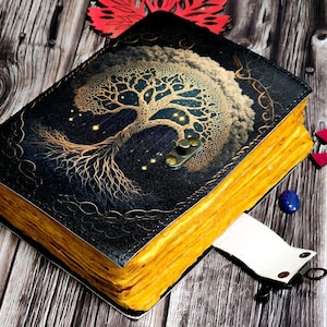 May include: A black leather journal with a gold tree design and a yellow spine. The journal has a metal clasp and a white ribbon bookmark.