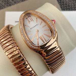 May include: A rose gold Bvlgari Serpenti watch with a teardrop-shaped case, a silver sunburst dial with Roman numeral indices, and a diamond-encrusted bezel. The watch features a flexible, coiled tubogas-style bracelet in polished rose gold.