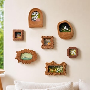 Puede incluir: Una colección de seis marcos de madera tallada pequeños con diversas formas y texturas, cada uno con una ilustración en miniatura. Los marcos presentan diseños orgánicos, irregulares y geométricos, mostrando escenas de flores, conejos y paisajes.