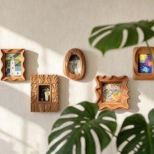 Könnte beinhalten: Eine Sammlung von fünf Holzbilderrahmen in verschiedenen Formen und Größen, die jeweils ein anderes Bild enthalten. Die Rahmen sind an einer hellen Wand befestigt, mit einer großen grünen Pflanze im Vordergrund.