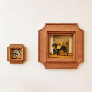 Puede incluir: Dos marcos de madera cuadrados con bordes decorativos. El marco más pequeño contiene una pintura de flores blancas en un jarrón. El marco más grande presenta una pintura de un caballo negro con una manta amarilla en un establo.