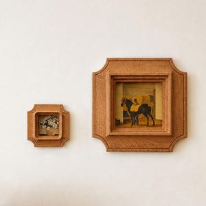 May include: Two wooden framed artworks hang on a white wall. One frame contains a painting of a horse and a man, the other a small floral arrangement. The frames have a decorative, scalloped edge.
