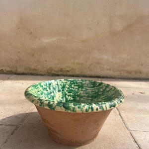 Puede incluir: Un pequeño cuenco de terracota hecho a mano con un interior moteado verde y crema. El borde está pintado de verde y el exterior es de color marrón natural. Este cuenco decorativo es adecuado para guardar objetos pequeños.