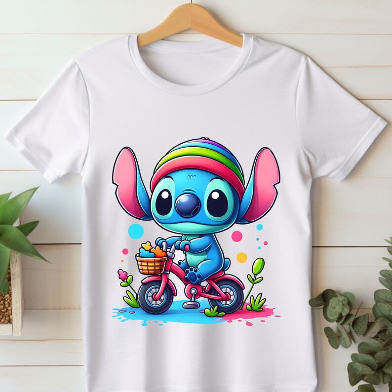 May include: White t-shirt with a cartoon blue Stitch character wearing a rainbow hat and riding a pink bicycle with a basket of flowers.