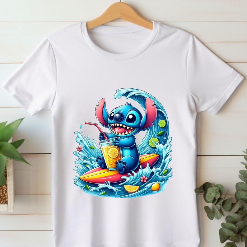 May include: White t-shirt with a blue cartoon character surfing on a wave. The character is holding a glass of lemonade and has a happy expression. The wave is blue and green with yellow lemons and flowers.
