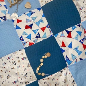 Könnte beinhalten: Eine blaue und weiße Patchwork-Babydecke mit einem Holzspielzeug und einem Holzschild mit der Aufschrift "loved".