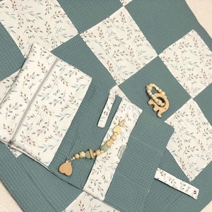 Könnte beinhalten: Eine babyblaue Spielmatte mit einem weißen und braunen Blumenmuster. Die Matte hat mehrere Taschen und eine Reißverschlusstasche. Ein Holz-Elefanten-Beißring und eine Perlenkette liegen auf der Matte.