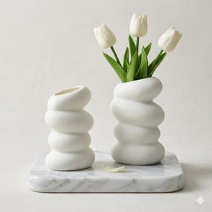Peut inclure: Un ensemble de trois tasses en céramique avec une finition mate et mouchetée. Les tasses sont de couleurs grise, blanche et noire. Chaque tasse a un design simple et moderne et une anse arrondie. Les tasses sont empilées.