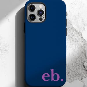 May include: A navy blue phone case with a black camera module. The case features the magenta letters "eb." at the bottom. The phone case is a solid color and has a smooth texture.