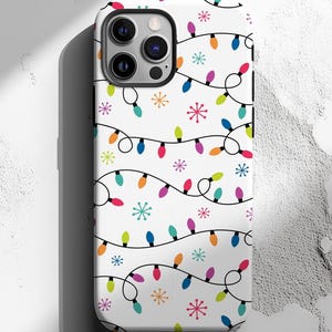May include: White phone case featuring a repeating pattern of colorful Christmas lights and snowflakes. The lights are in various colors, including red, blue, green, and yellow, with black wiring. The case has a glossy finish.