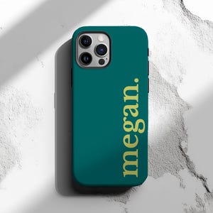 May include: Teal phone case with the name "megan." in gold lettering. The case has a smooth finish and a camera cutout. The phone case is designed to fit a smartphone.