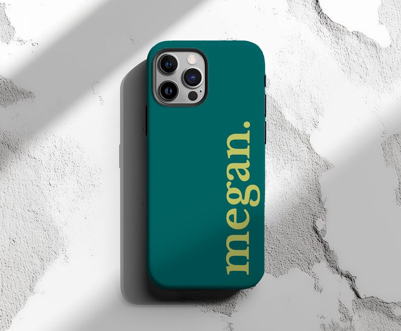 May include: Teal phone case with the name "megan." in gold lettering. The case has a smooth finish and a camera cutout. The phone case is designed to fit a smartphone.