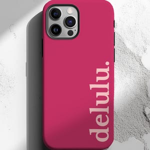 May include: A magenta phone case with the word "delulu" printed vertically in a light beige color. The case has a black border around the camera and a shadow on the left side.