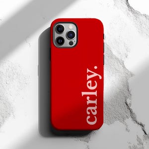 May include: A bright red phone case with the name "carley." printed vertically in white. The case has a sleek design and a camera cutout. The background is a textured white surface.