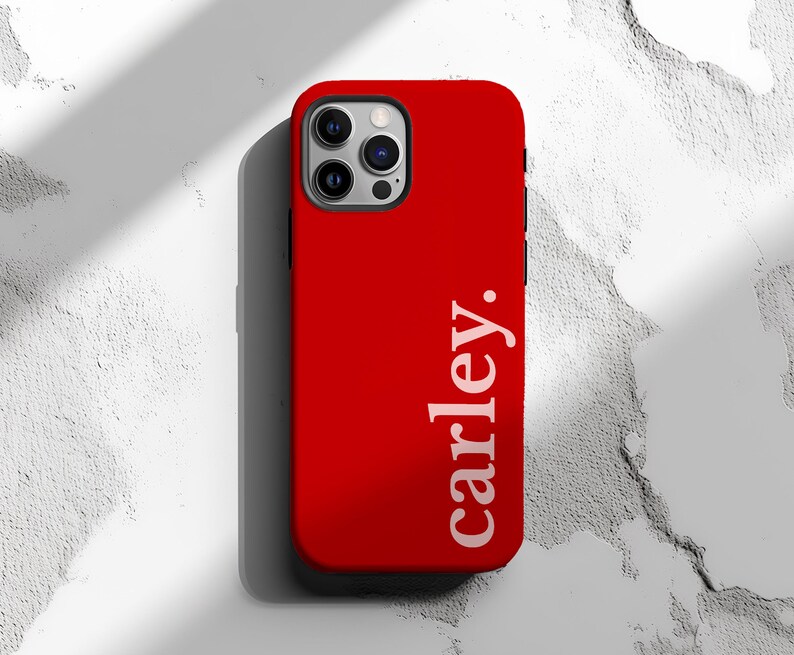 May include: A bright red phone case with the name "carley." printed vertically in white. The case has a sleek design and a camera cutout. The background is a textured white surface.