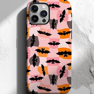 May include: A phone case featuring a repeating pattern of black bats on a pink, orange, and gray patchwork background. The case has a glossy finish and a camera cutout.