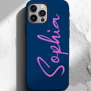 May include: A navy blue phone case with the name "Sophia" in a pink cursive font. The case has a black border and a camera cutout. The phone case is designed to fit a smartphone.