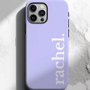 May include: A lavender phone case with the name "rachel." printed vertically in white. The case has a black camera module and buttons on the side. The phone case is on a white and gray textured surface.