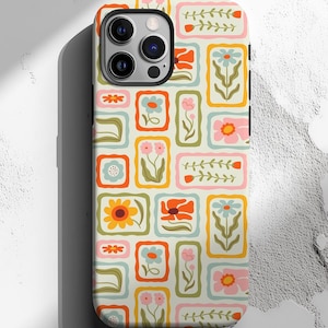May include: A phone case with a colorful floral pattern. The design features rectangular frames with various flowers in orange, pink, blue, and yellow on a cream background. The case has a black border and a camera cutout.