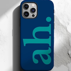 May include: A navy blue phone case with the teal letters "ah." The phone case has a dark blue border and a camera module with three lenses. The case is on a white and gray textured surface.