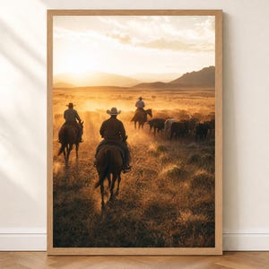 May include: A framed vertical wall art print depicting a golden hour scene of three riders on horseback herding a group of cattle across a dusty, dry landscape with distant mountains under a bright, hazy sunlit sky.