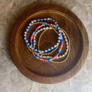 May include: A set of colorful beaded bracelets with gold accents. The bracelets are stacked on a wooden surface.