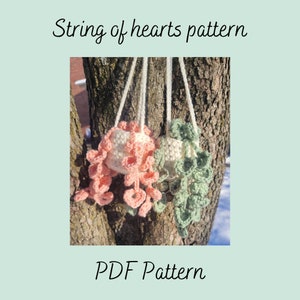 Puede incluir: Dos maceteros colgantes de ganchillo, uno rosa y otro verde, con el texto "String of hearts pattern" y "PDF Pattern" en la imagen.