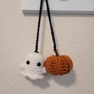 May include: A white crocheted ghost and an orange crocheted pumpkin hanging from a black cord.