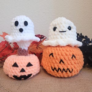 May include: Two crocheted Halloween decorations. One is a pumpkin with a ghost face on top. The other is a pumpkin with a ghost face on top. Both pumpkins are orange and the ghosts are white.