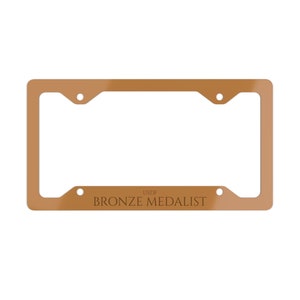 May include: A gold-colored license plate frame with the text "USDF BRONZE MEDALIST" printed on the bottom.