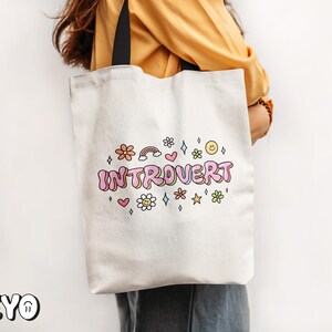 May include: White tote bag with black handles and the text "Introvert" in pink and rainbow letters with colorful flowers and stars around it.